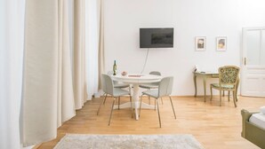 A modern living room with a round dining table, grey chairs, a flat-screen TV mounted on the wall, and a small side table with a laptop. - Best of Hernals Top 24 (Vienna)