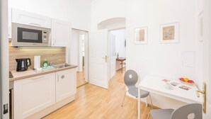 A modern kitchen with white cabinets, a microwave, and a coffee maker. There is a dining area with a table and chairs. - Best of Hernals Top 30 (Vienna)