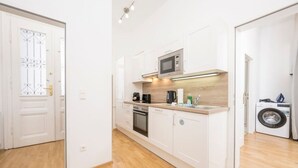 A modern kitchen with white cabinets, a microwave, a coffee maker, and a washing machine. - Best of Hernals Top 30 (Vienna)