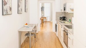 A narrow kitchen with a dining area, wooden flooring, and white cabinetry. - Best of Hernals Top 34 (Vienna)