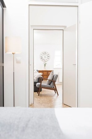 A modern, minimalist room with a white door leading to a living area featuring a grey sofa and a wooden side table. - Anna and Friends Top 17 (Graz)