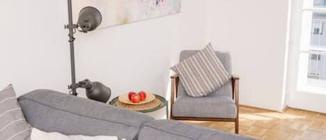 A modern living room with a gray sofa, a floor lamp, a chair, and a colorful abstract painting on the wall.