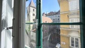 A view through a window with a green frame, looking at a street with buildings and a sign that reads "Judenplatz."