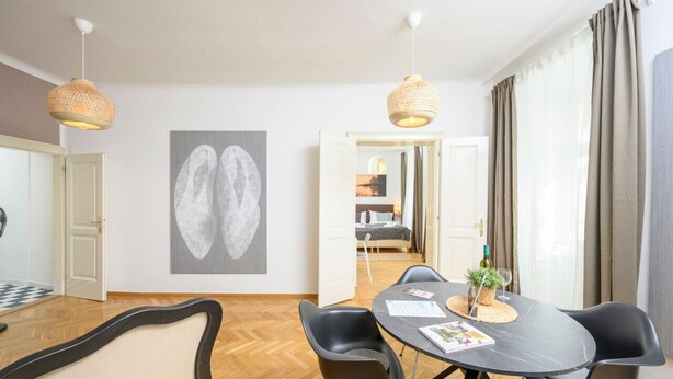 A modern hotel room with a dining area, a large abstract painting, and a view into the adjacent bedroom.