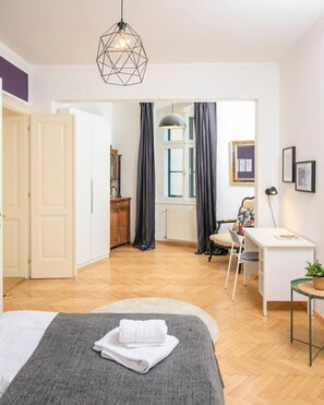 Un dormitorio moderno con una cama, un escritorio y una silla. Hay una ventana con cortinas, un radiador y una puerta que da a otra habitación.