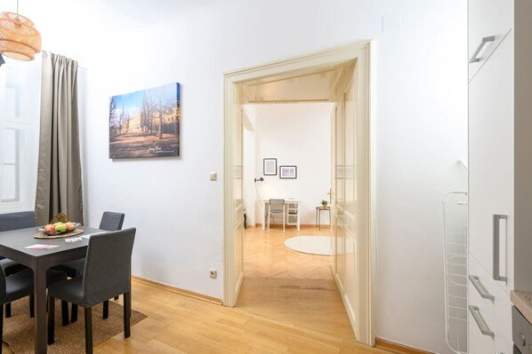 Una habitación moderna con una mesa de comedor, sillas, una mesita con una silla, un cuadro en la pared y una puerta que da a otra habitación.