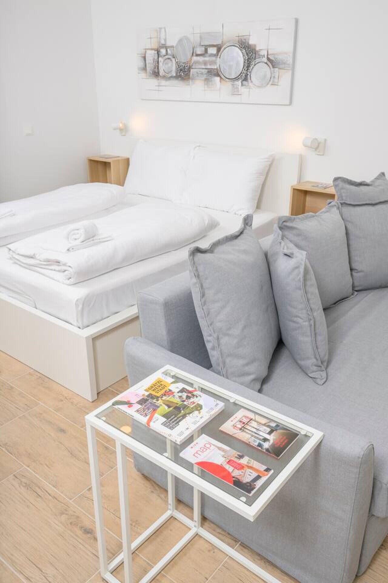 A bedroom with a bed, a grey sofa, and a small table with magazines.