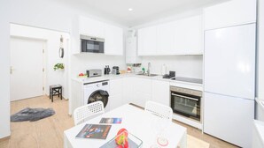 Une cuisine moderne avec des armoires blanches, un four à micro-ondes, un four et un réfrigérateur. On y trouve une table à manger avec des chaises et un tapis sur le sol.