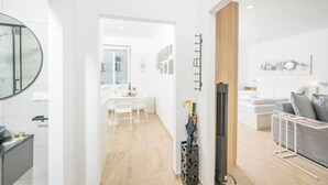 Un appartement moderne comprenant une cuisine, un coin repas et un salon. Il y a une télévision, un porte-manteau et une fenêtre avec des stores.
