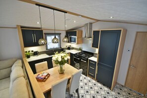A compact kitchen with modern appliances, a dining area with a table and chairs, and a sofa. - Tranquility at Pendle view holiday Park (Clitheroe)