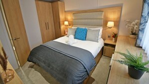 Une chambre d’hôtel bien aménagée, avec un grand lit, une armoire en bois, des lampes de chevet et une petite table agrémentée d’une plante.