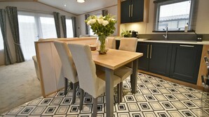 Une cuisine moderne avec des meubles de couleur sombre, un plan de travail en bois et un évier. On y trouve un coin repas avec une table et des chaises, ainsi qu'un vase rempli de fleurs posé sur la table.