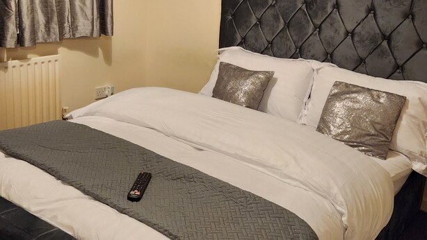 A neatly made bed with a black headboard, a grey quilt, and a remote control on the bed. - Captivating 3-bed House in Kent (Erith)