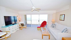 A hotel room with a TV, white furniture, a red chair, a white sofa, and a balcony with a view. - Beachmark 4K-Oceanfront 73rd St, WIFI, Pool, Elev, W/D, AC (Ocean City)