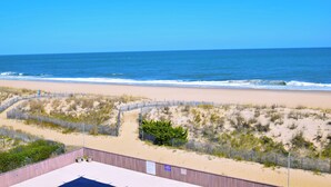 A beach view from a building with a wooden deck, sandy dunes, and a fence. - Beachmark 4K-Oceanfront 73rd St, WIFI, Pool, Elev, W/D, AC (Ocean City)