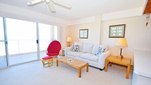A living room with a white sofa, a red chair, a wooden coffee table, and two side tables with lamps. - Beachmark 4K-Oceanfront 73rd St, WIFI, Pool, Elev, W/D, AC (Ocean City)