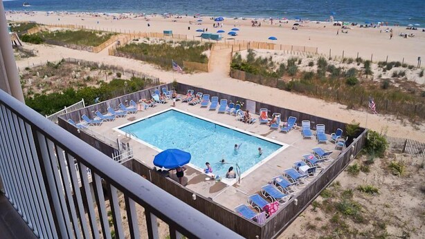 A pool area with lounge chairs and a view of the beach. - Beachmark 4K-Oceanfront 73rd St, WIFI, Pool, Elev, W/D, AC (Ocean City)
