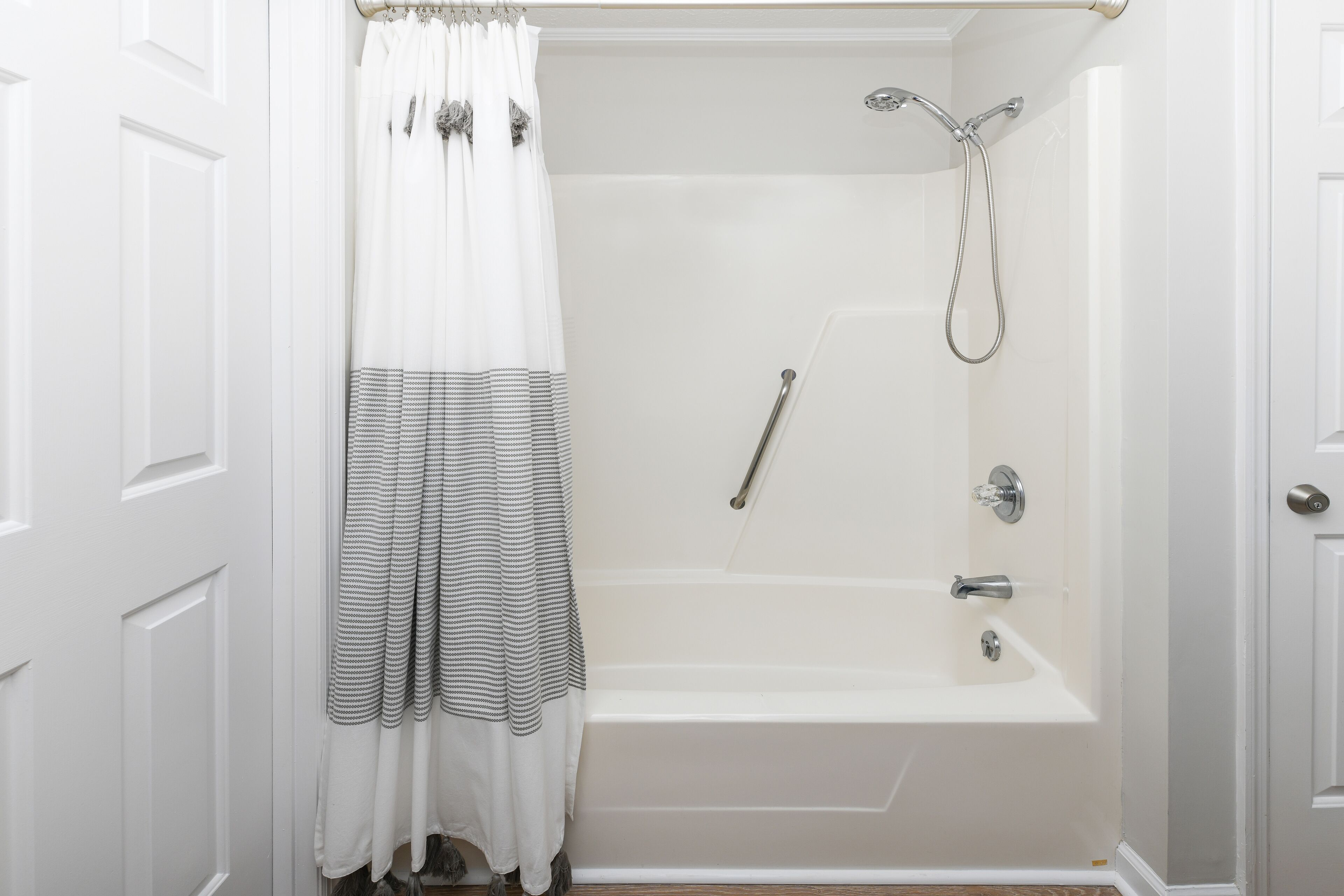 Un baño con una bañera blanca, una ducha con cabezal de ducha manual y una cortina a rayas.