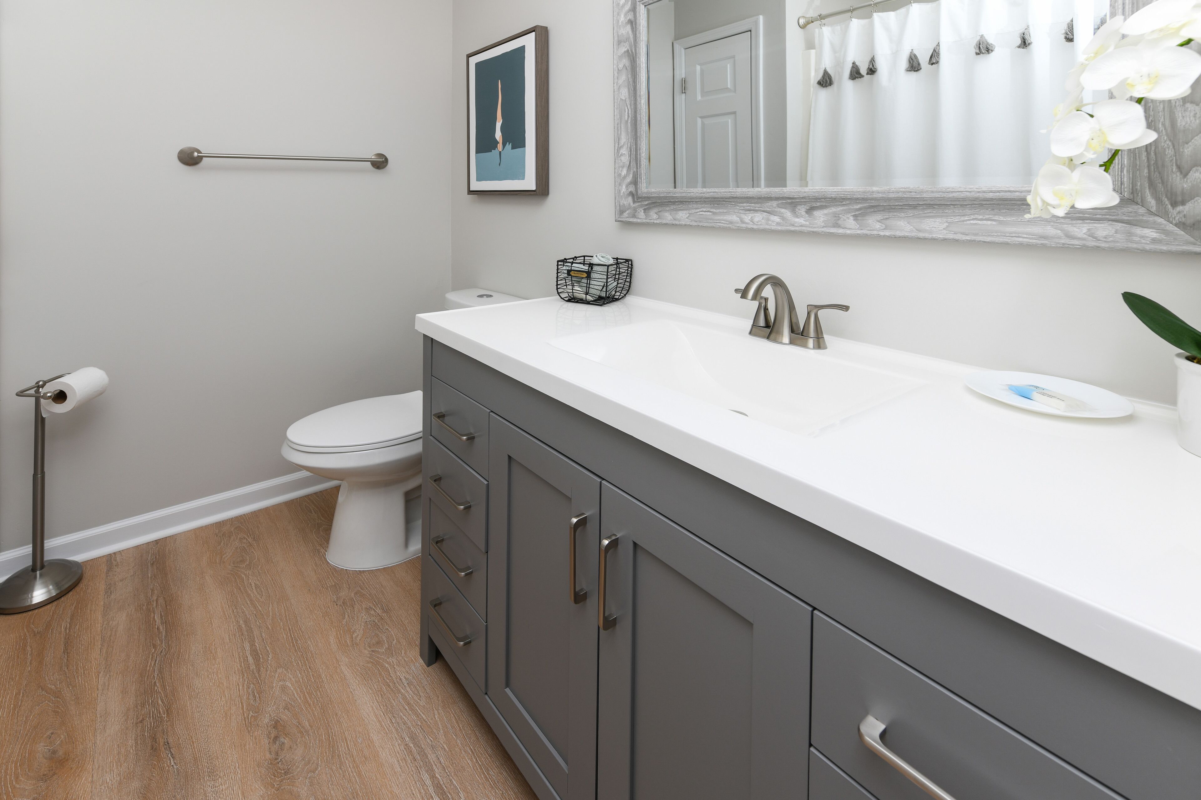 A bathroom with a white sink, dark gray cabinets, a white toilet, and a wooden floor.