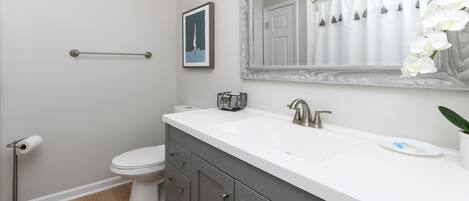 A bathroom with a white sink, dark gray cabinets, a white toilet, and a wooden floor.