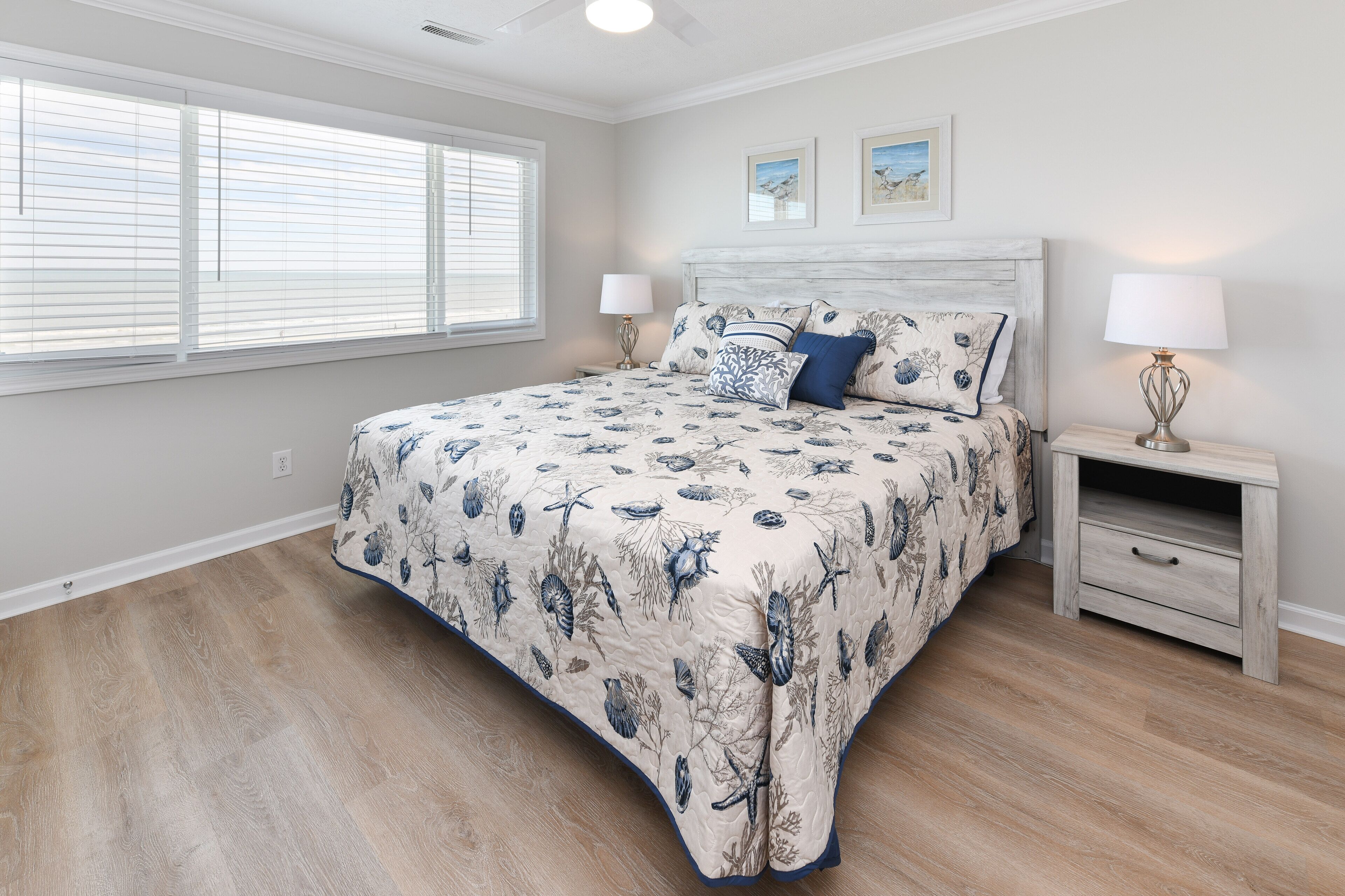 A bedroom with a large bed, two bedside tables, a nightstand, and a window with blinds.