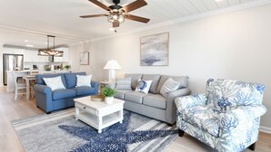 Ein modernes Wohnzimmer mit Deckenventilator, einem blauen Sofa, einem grauen Sofa, einem gemusterten Sessel und einem Couchtisch.