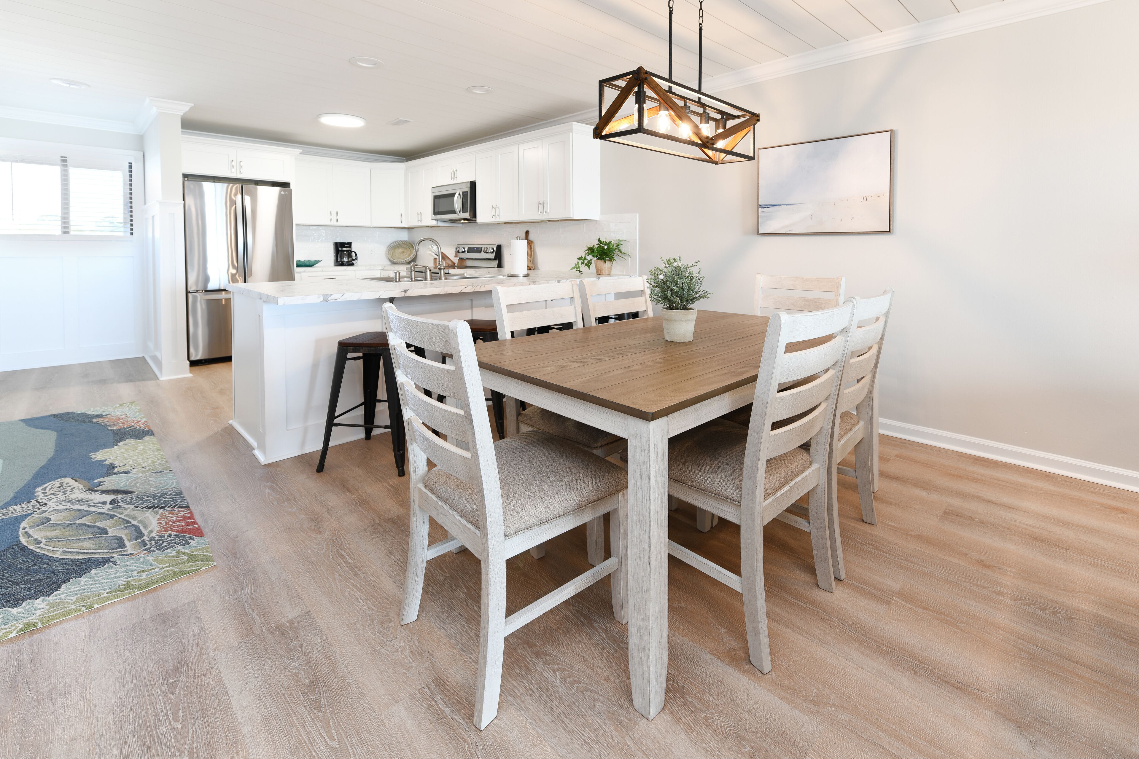Une cuisine moderne avec des meubles blancs, un réfrigérateur en acier inoxydable et une table à manger en bois, accompagnée de chaises.