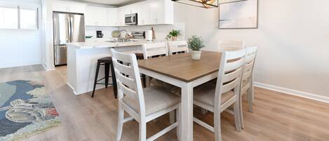 Une cuisine moderne avec des meubles blancs, un réfrigérateur en acier inoxydable et une table à manger en bois, accompagnée de chaises.