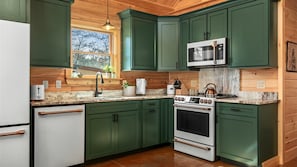 A kitchen with green cabinets, a white refrigerator, a stainless steel microwave, a gas stove, and a wooden ceiling.