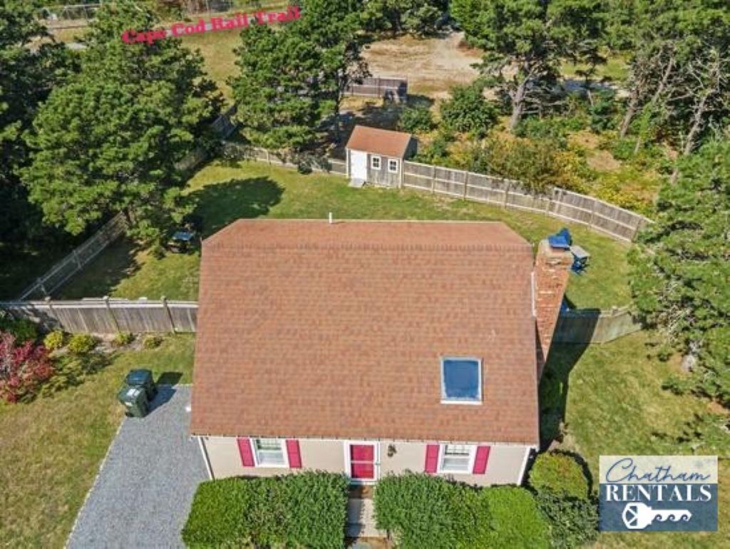 Una casa de dos pisos con techo rojo, un garaje pequeño adosado y un patio cercado.