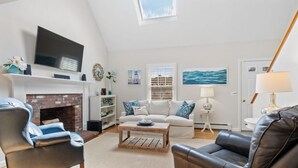 A living room with a fireplace, a television, and a sofa. - Wonderful dog friendly rental with access path to a private beach deeded at White's Pond! (Chatham)