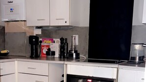 Eine Küche mit weißen Schränken, einem schwarzen Backofen, einer Kaffeemaschine und einem Mülleimer.