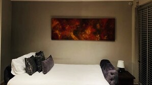 Ein Hotelzimmer mit einem großen Bett, einem Nachttisch, einer Lampe und einem Gemälde an der Wand.