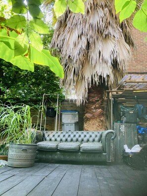 A wooden deck with a tufted leather sofa, a large potted plant, and a thatched roof structure. - Sanctuary Place in the Heart of London (London)