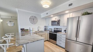 A modern kitchen with stainless steel appliances, a large clock, and a bar area with stools.