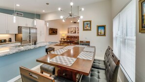 A modern kitchen with a central island, built-in appliances, pendant lighting, and a dining area with a large table and cushioned seating. - Daytona Beach Vacation Home ~ 4 Mi to Main St Pier (Holly Hill)