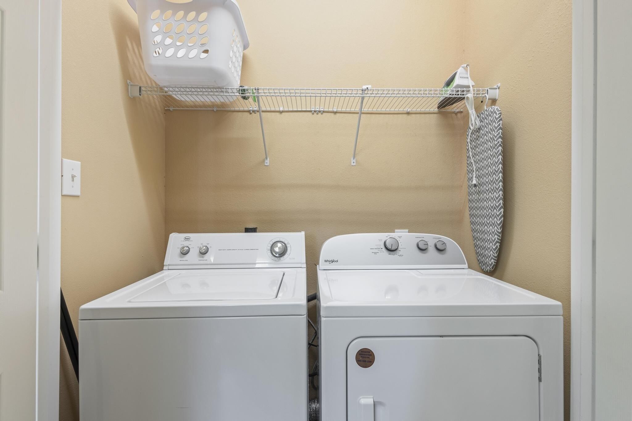 A laundry room with two white front-loading washers and dryers, a drying rack, and a hanging iron.