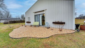A single-story building with a large window and a door, surrounded by a gravel patio with two chairs and a small plant. - Missouri Couple's Retreat: 'shouse' w/ Patio, Yard (Nixa)