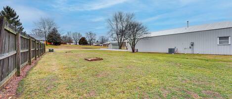 A grassy yard with a wooden fence, a shed, and a large building with a flat roof.