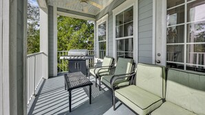 Een overdekte veranda met een plafondventilator, een barbecue en twee groene fauteuils.
