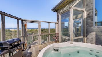 A wooden deck with a hot tub, a grill, and a chair overlooking a scenic view.
