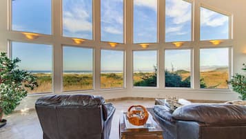 A room with large windows offering a view of a grassy landscape. There are two leather sofas and a small table with a decorative bowl.