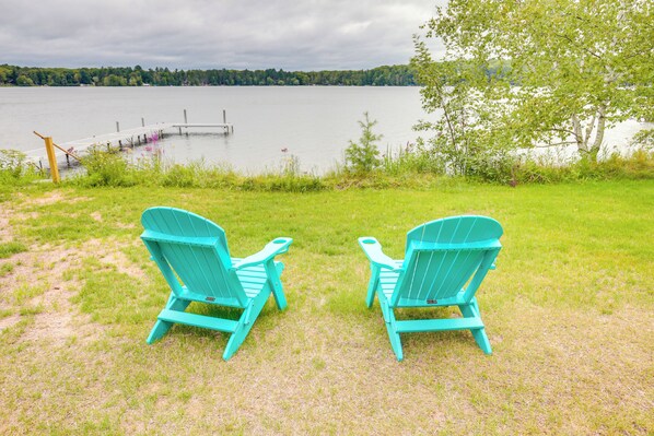 Two turquoise Adirondack chairs facing a lake with a dock and a tree in the background. - Lakefront Rhinelander Cottage w/ Private Dock! (Rhinelander)