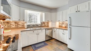 Uma cozinha moderna com armários brancos, lava-louças embutida, fogão de aço inoxidável e geladeira.