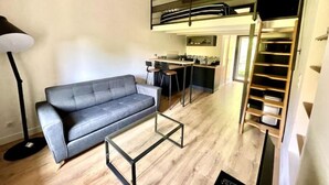 A modern living room with a grey sofa, a glass coffee table, and a kitchen area with a mezzanine.