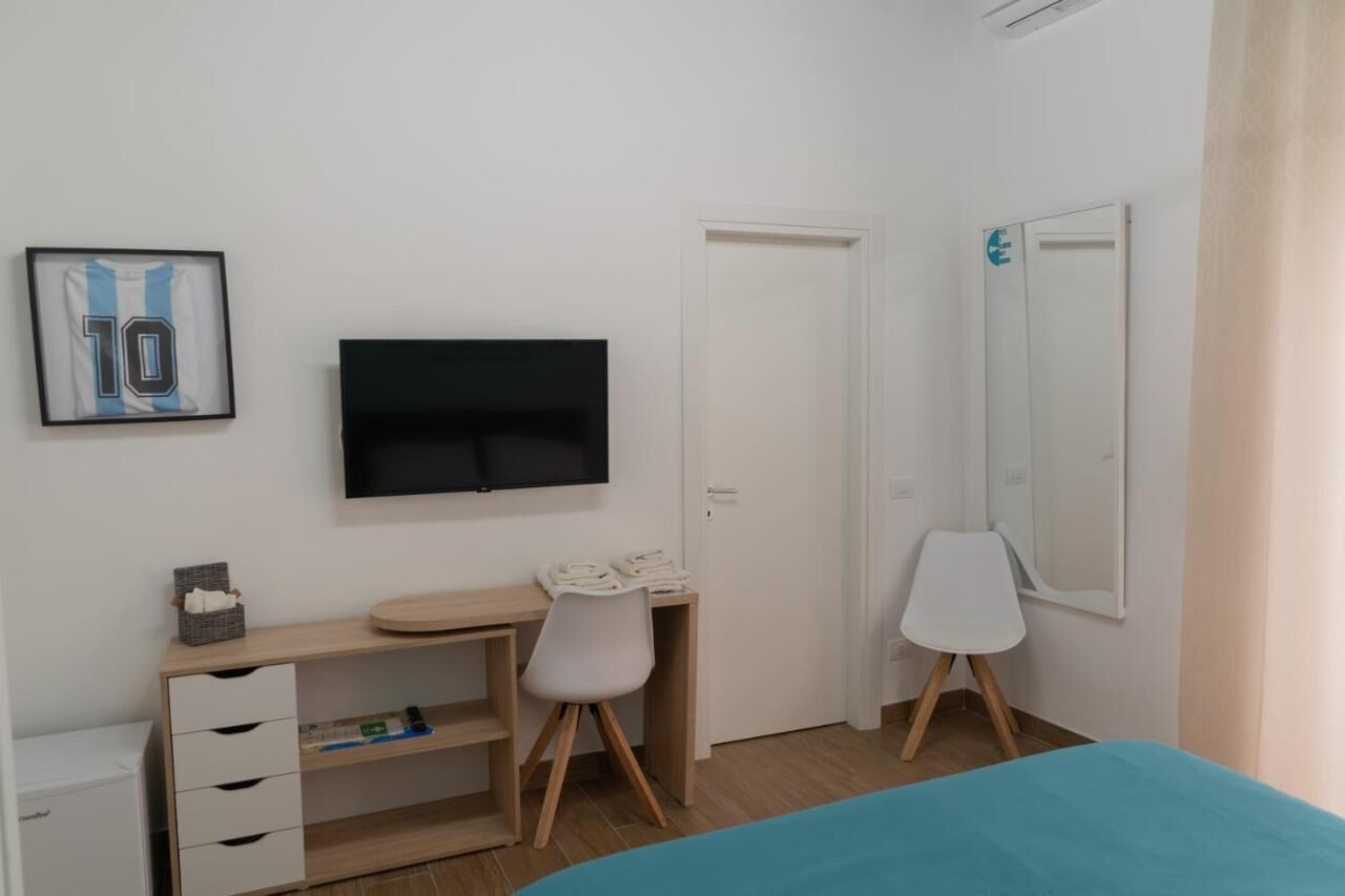 A bedroom with a bed, a desk with a chair, a TV, a wardrobe, and a mirror.