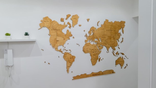 Mapa-múndi de madeira numa parede branca, com uma pequena prateleira e um telemóvel.