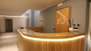 A reception desk with a wooden finish and a glass top, a wooden door with a logo, and a vase with sticks on the wall. - Ro agrimaison  (Volla)