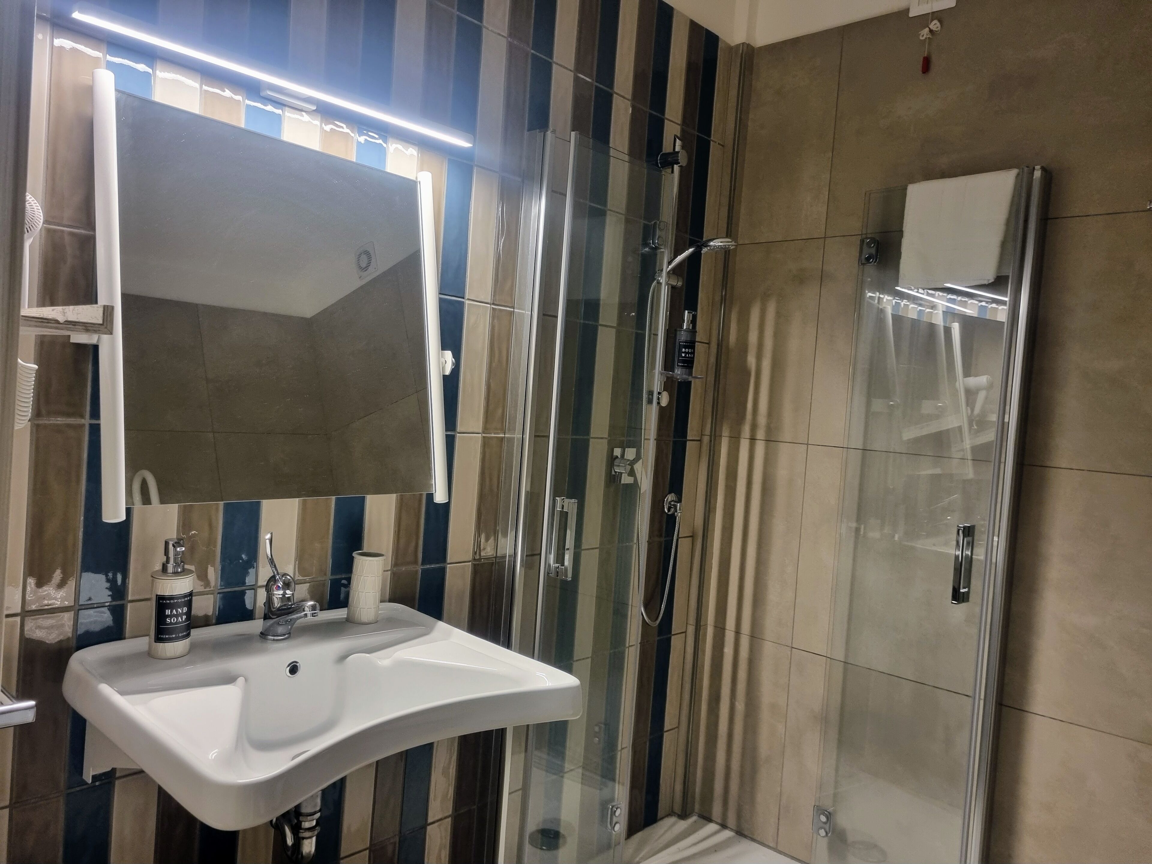 Ein modernes Badezimmer mit einer gläsernen Duschkabine, einem weißen Waschbecken und einem Spiegel darüber.