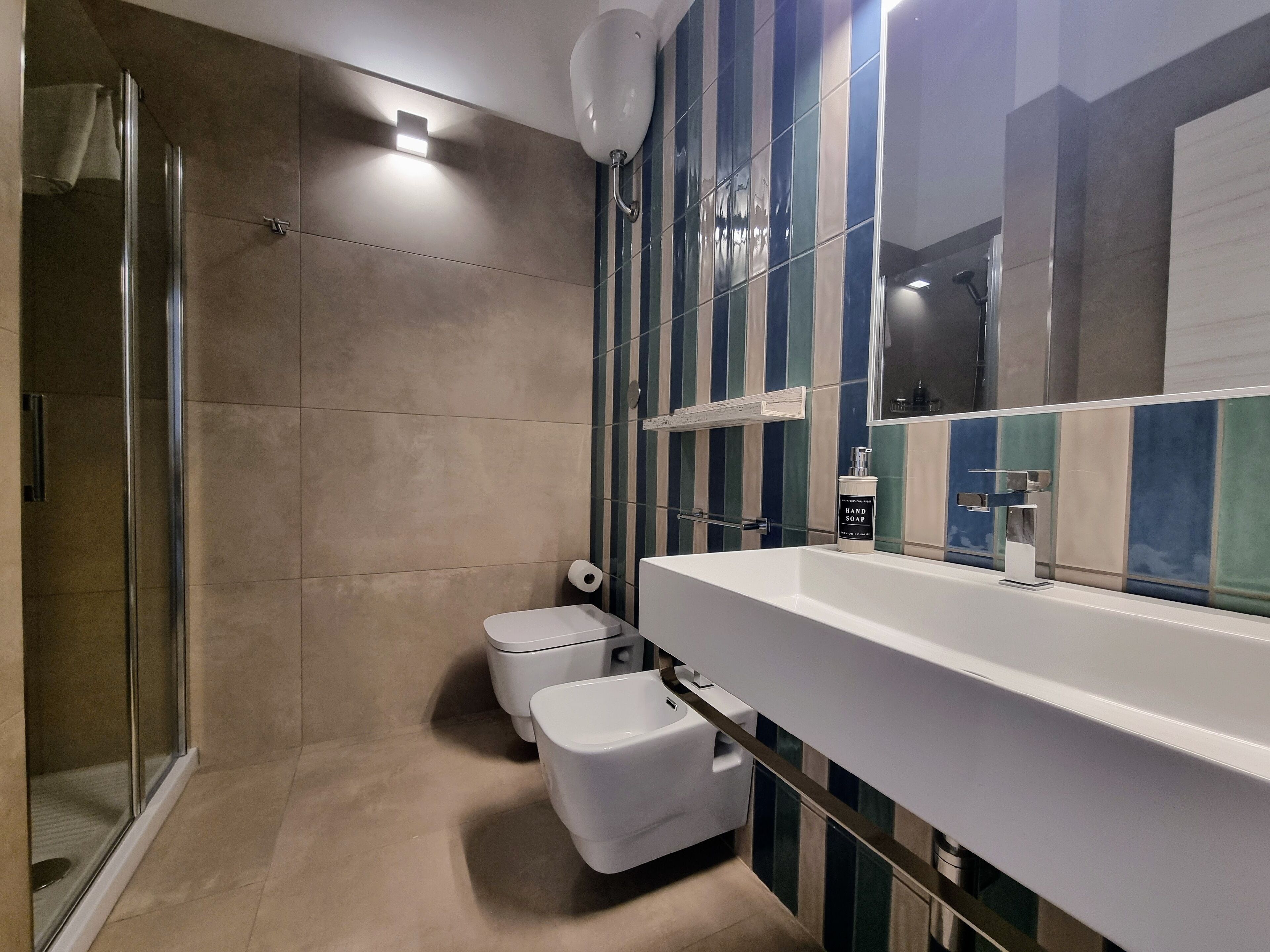 A modern bathroom with a glass shower enclosure, a white sink with a large mirror, and a toilet with a white lid.